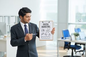 Man explaining why hire a digital marketing agency. https://www.freepik.com/free-photo/man-suit-standing-office-with-clipboard-pointing-poster-with-words_5576504.htm#fromView=search&page=1&position=13&uuid=695af754-e55d-40e2-81b7-59ba595580f5